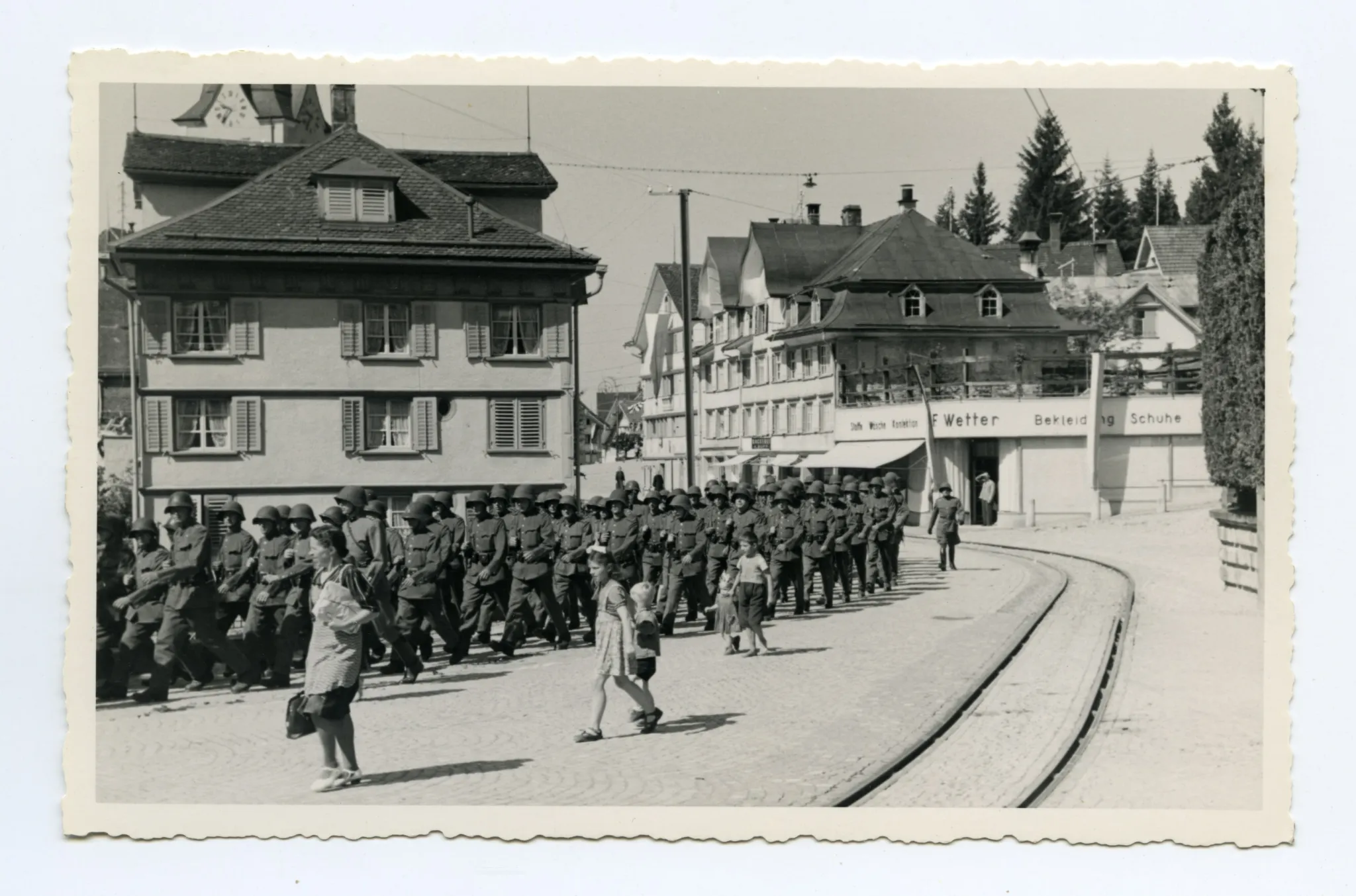 Soldaten marschieren auf der Hauptstrasse Richtung ZeughausBahnhofskreuzung, im Hintergrund Bekleidungsgeschäft F. Wetter