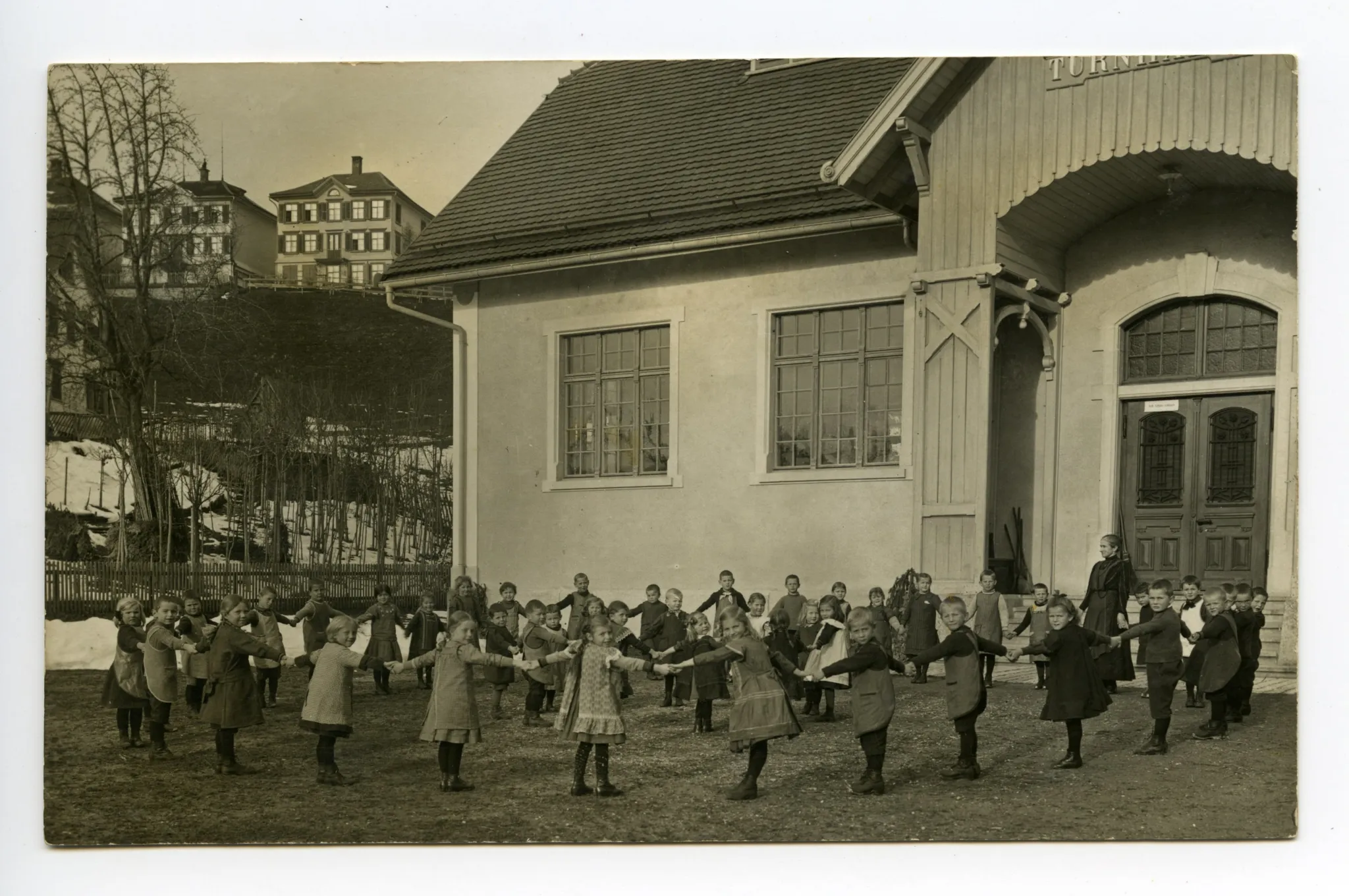 Kinder im Kinderreigen vor der Turnhalle mit Lehrperson
