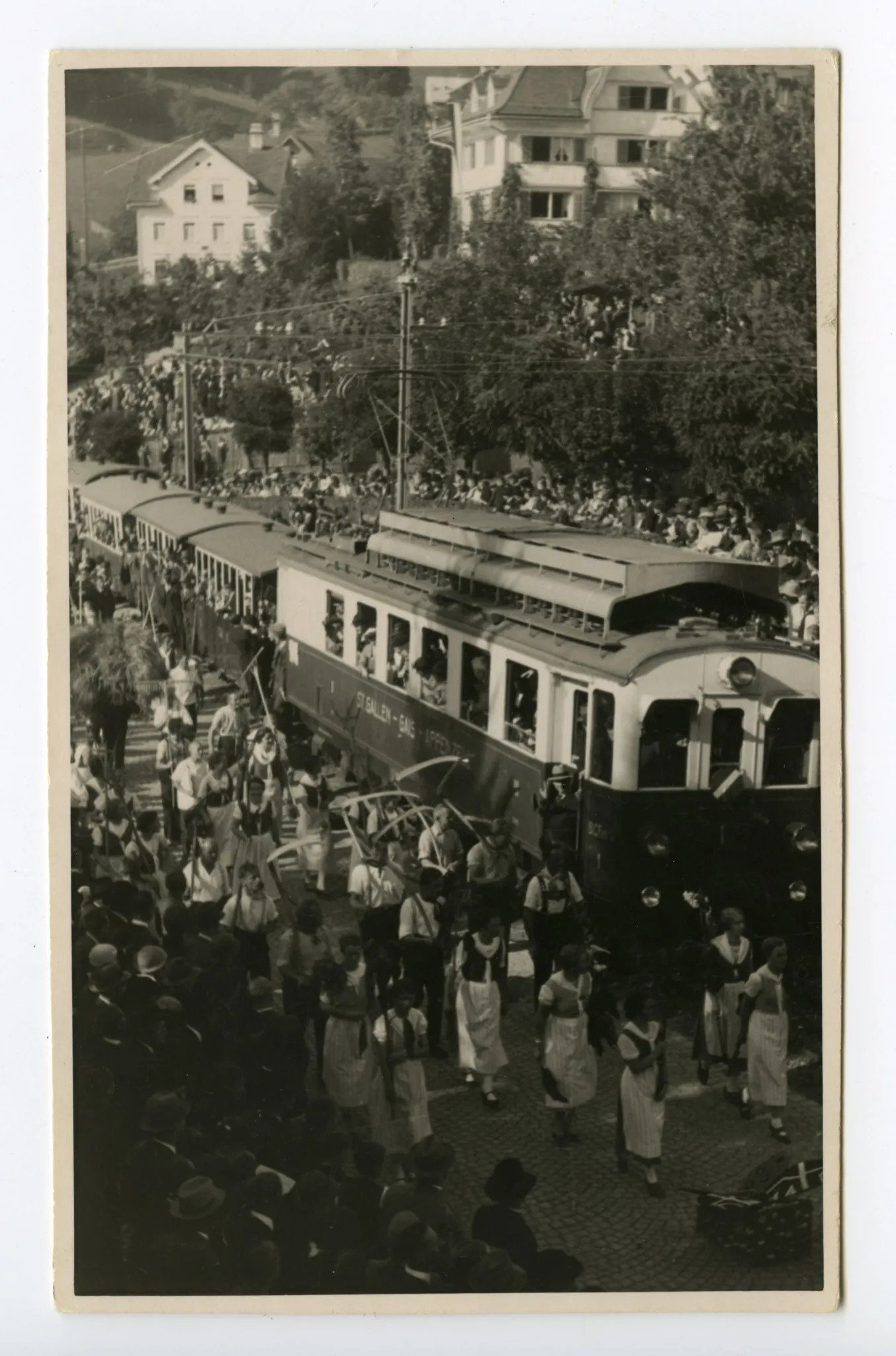 Gruppe der Bauern mit Sense und Bäuerinnen mit Rechen in der Kurve zum alten Bahnhof, fahrende Bahn (SGA)