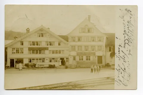Metzgerei im Februar 1980 eingegangen, Drogerie 1966 eingegangen, Frontansicht mit Personen davor, Ochse wird vor der Metzgerei gehalten, Eisenbahnschienen im Vordergrund sichtbar, Drogerie G. Moesch mit im Bild