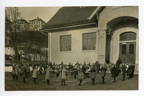 Kinder im Kinderreigen vor der Turnhalle mit Lehrperson