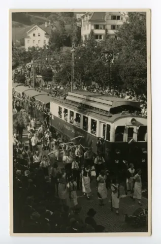 Gruppe der Bauern mit Sense und Bäuerinnen mit Rechen in der Kurve zum alten Bahnhof, fahrende Bahn (SGA)