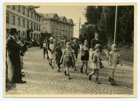 Gruppe von Kindern (Schüler)auf der Hauptstrasse gehend, Kinder mit Chränzen und Beerenkörgen, im Hintergrund Druckerei Kunz